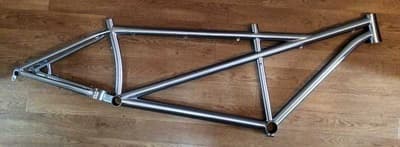 A bare titanium tandem frame on a wooden floor